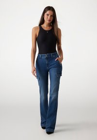 Cuerpo sin mangas negro combinado con pantalones cargo de mezclilla de tiro alto en un azul desgastado, con bolsillos laterales y un diseño de pierna amplia.