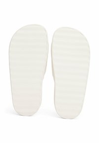 Suela de zapatos de goma blanca con un patrón texturizado y a rayas. Marca "TOMMY HILFIGER" grabada. Acabado suave con una forma redondeada.