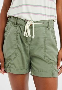 Shorts en coton vert olive avec taille à cordon, ourlet roulé et poches avant. Présente des coutures contrastées et une texture douce.