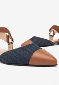 Zapatos planos de cuero marrón y denim con punta afilada, tira en el tobillo y materiales contrastantes. Incluyen una textura suave en la punta.