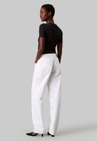 Sort tætsiddende kortærmet bluse parret med løse hvide jeans. Sorte hæle. Minimalistisk design med glat tekstur og subtile detaljer.