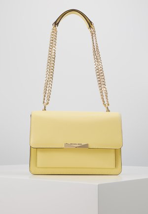 Żółta skórzana torebka na ramię z złotym łańcuszkowym paskiem i plakietką z logo Michael Kors na przednim klapie, wystawiona na białym piedestale.