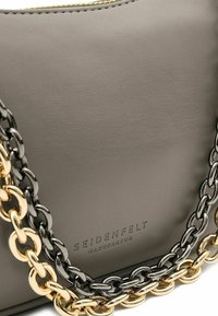 Borsa in pelle grigia con superficie testurizzata, dettagli in catena oro e nera e logo in rilievo. Chiusura con cerniera nella parte superiore.