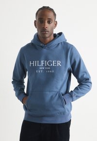 Felpa blu con logo; materiale in cotone, tasca frontale, cappuccio regolabile, polsini e orlo a costine, presenta un piccolo logo sulla manica.