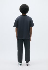 Grå bomulds T-shirt med korte ærmer, parret med mørkegrå bukser og hvide sneakers. Glat tekstur, enkelt design, ingen synlige mønstre.