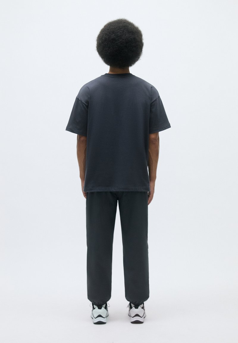 T-shirt grigia in cotone con maniche corte, abbinata a pantaloni grigio scuro e sneakers bianche. Texture liscia, design semplice, senza motivi visibili.