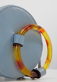 Borsa a mano circolare in pelle blu con manico in acrilico giallo e arancione brillante, caratterizzata da cuciture a contrasto e una superficie liscia.