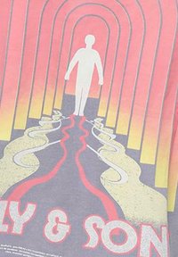 Camiseta gris con un diseño gráfico de una figura blanca rodeada de arcos coloridos en rojo, naranja y amarillo, con líneas onduladas en la parte inferior.