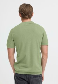 Polo à manches courtes en tissu tricoté vert clair avec un col, des coutures visibles et des poignets côtelés, vu de dos.