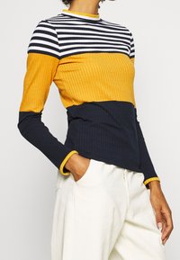 Geripptes Langarmoberteil mit einem Farbblockdesign: gestreifter navy-weißer oberer Bereich, senfgelber Mittelteil und unifarbener navy unterer Bereich.