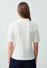 Witte polo met korte mouwen van een ribbelstructuur en een subtiel ruitpatroon, met een klassieke kraag en een getailleerde pasvorm.