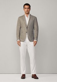 Blazer en lin gris clair avec deux poches avant, associé à un pantalon blanc et des chaussures en cuir marron. Fermeture à boutons et coupe ajustée.