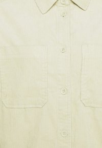 Chemise en velours côtelé crème avec deux poches plaquées devant, quatre boutons au centre et un col pointu.