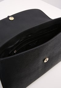 Svart texturerad handväska med glansig yta, utrustad med en metallknäppning och en välorganiserad insida med flera fack.