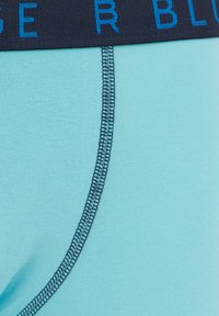 Svetlo modra moška spodnja perila z temno modrim elastičnim pasom, ki vključuje kontrastno napisano besedilo in gladek, raztegljiv material.