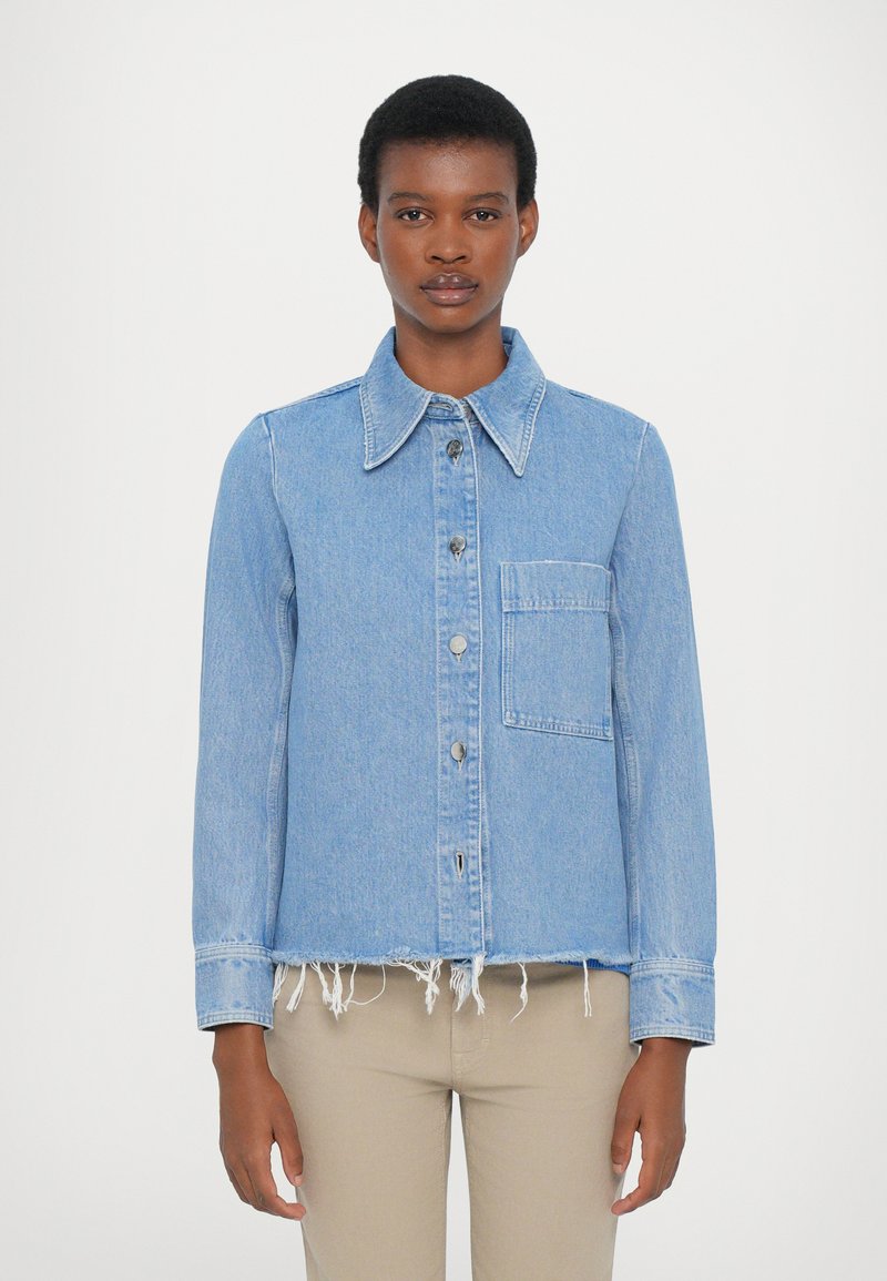 Light blue denim jacket with a collared neckline, front pocket, visible stitching, and frayed hem. Button closure and long sleeves.