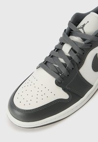 Hallide ja valged nahksneakerid perforatsiooniga varbakast, ümmargused paelad ning eristuv Swoosh logo. Omab tekstuurilisi aktsente ja tugevat tallat.