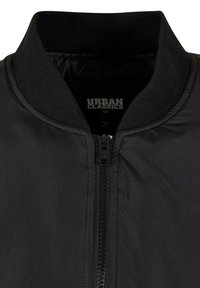 Chaqueta bomber negra con cierre de cremallera, cuello acanalado y diseño minimalista. La etiqueta interior indica "Urban Classics" y la talla "M."
