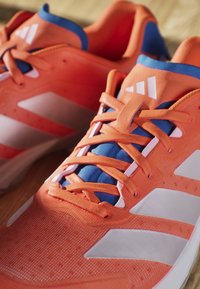 Scarpe da corsa arancioni vivaci con strisce bianche e linguetta blu, con lacci arancioni e tomaia in tessuto strutturato.