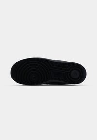 Semelle noire de basket avec motifs de bande de roulement circulaires et petit logo Nike au centre sur fond blanc uni.
