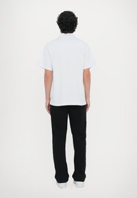 Kortermet hvit polo med krage, kombinert med sorte bukser. Stoffet ser glatt ut; passformen er uformell og avslappet.