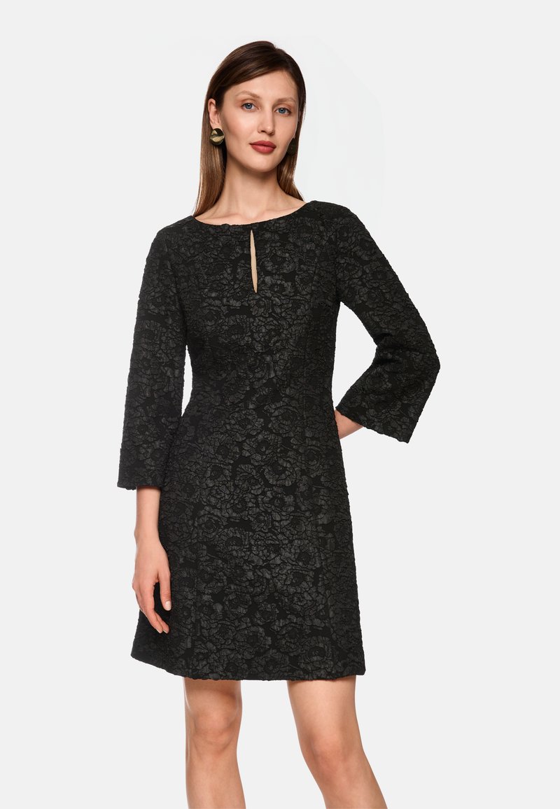 Schwarzes Spitzenkleid mit Rundhalsausschnitt und Schlüssellochdetail, mit drei Viertel langen Ärmeln und einer figurbetonten Silhouette.