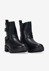 Botines negros de tobillo hechos de material suave, con hebillas laterales, un tacón robusto, suela texturizada y cierre de cremallera para facilitar su uso.