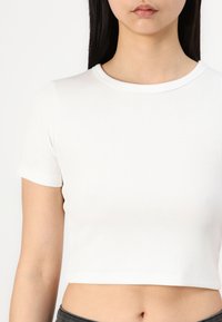 Balts ribots īsām piedurknēm cropped tops ar apaļu izgriezumu, kas izceļ cieši pieguļošu dizainu un gludu tekstūru.