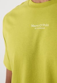 Svetlozelené bavlnené tričko s okrúhlym výstrihom, krátkymi rukávmi a bielym potlačeným textom "Marc O'Polo EST. IN STOCKHOLM."