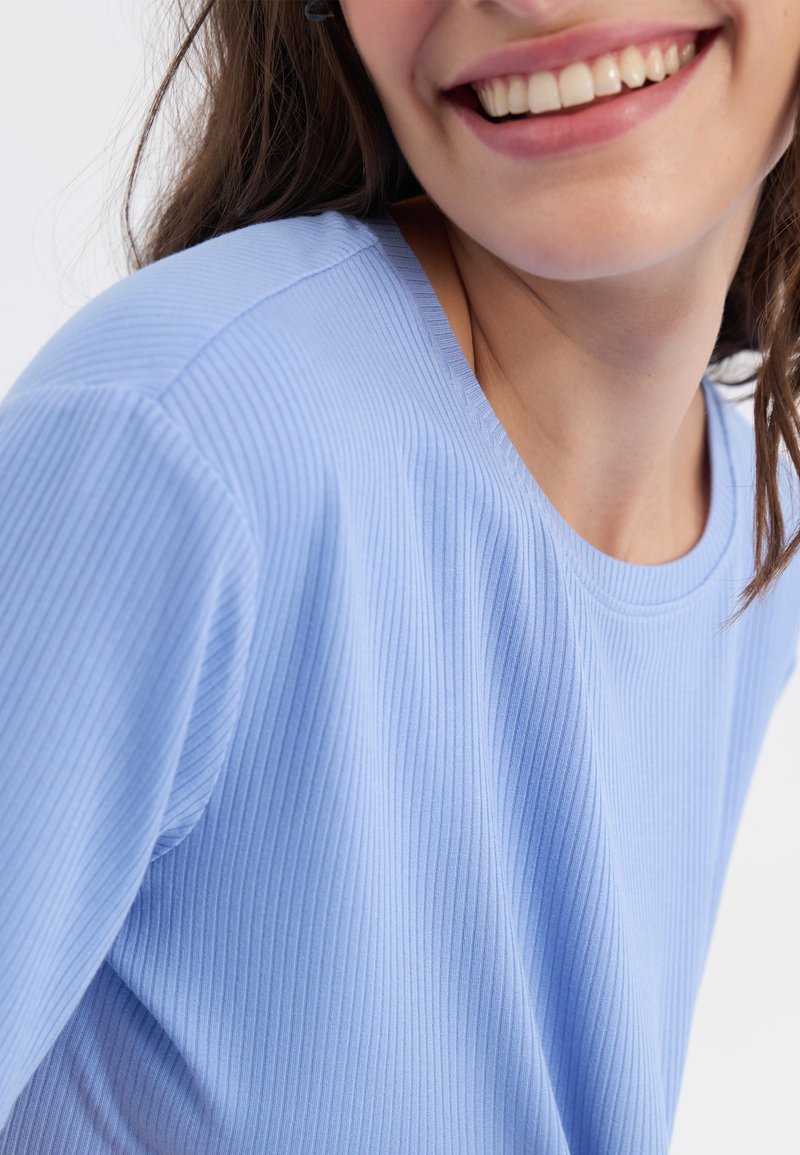 Maglietta a maniche corte azzurro chiaro a coste, con colletto rotondo, caratterizzata da una texture morbida e sottili righe verticali.