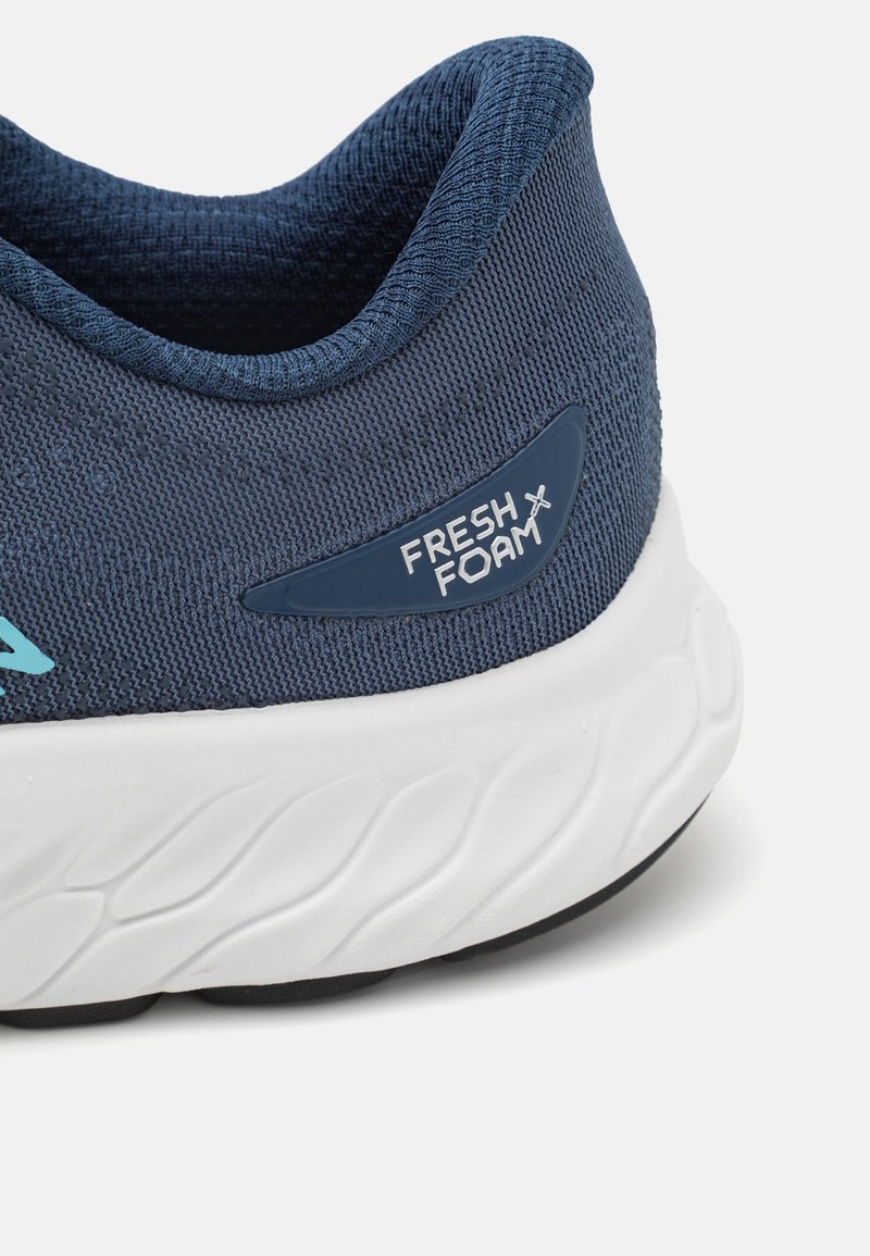 Eine Nahaufnahme der Ferse eines navyblauen Sneakers mit strukturiertem Material, weißer Sohle und dem "FRESH FOAM"-Logo an der Seite.