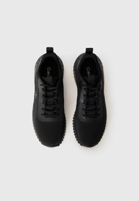 Zwarte sportieve schoenen met een bovenwerk van mesh, rubberen zool en vetersluiting. Gladde accenten en branding zijn zichtbaar aan de binnenkant.