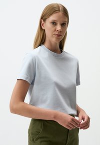 T-shirt di cotone azzurro chiaro con scollatura rotonda e maniche corte, caratterizzata da una texture liscia e una vestibilità comoda. Abbinato a pantaloni verdi.