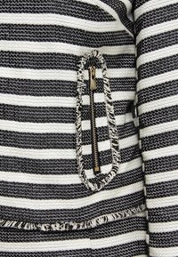 Czarno-biała tkanina w paski z fakturowanym wzorem. Zawiera małą kieszeń na suwak z detalami z frędzlami.