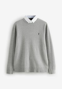 Grå strikket sweater med rund hals og en hvid skjorte under. Har et lille marineblåt logo på brystet og ribbede manchetter.