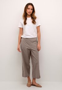T-shirt blanc à manches courtes, pantalon large gris clair avec fentes sur les côtés, et ballerines beiges. Tissu lisse avec des lignes simples et une coupe décontractée.