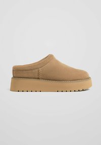Tan suede slip-on shoes with a rounded toe, padded collar, and a thick, textured beige sole featuring a ridged pattern.