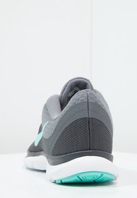 Zapatilla deportiva gris con parte superior de malla texturizada, detalles en turquesa y suela blanca. Presenta una puntera redondeada y un talón acolchado.