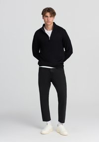 Maglione nero in maglia con colletto a zip quarti, abbinato a pantaloni neri tapered e sneakers bianche, realizzato in un tessuto testurizzato.