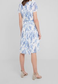 Blommig klänning med korta ärmar, ljusblå och vit färgkombination, åtsittande midja, knälång kjol och texturerad tyg.