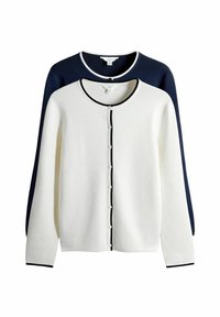 Cardigan alb cu garnitură și nasturi negri în față, purtat peste un fundal texturat bleu închis. Mâneci lungi, decolteu rotund.