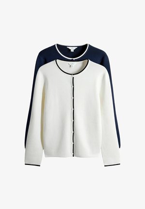 Fehér kardigán fekete szegéllyel és gombokkal az elején, sötétkék, texturált háttér előtt rétegezve. Hosszú ujjú, kerek nyakkivágással.