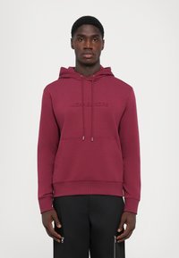 Burgunderfarget hettegenser i mykt stoff med frontlomme og preget "Michael Kors"-logo. Har justerbare snorer og ribbestrikkede mansjetter.