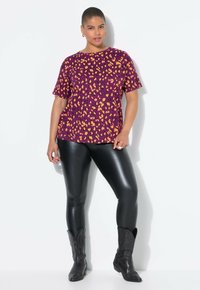 Camiseta corta de manga morada con estampado de leopardo naranja, combinada con leggings negros brillantes y botas vaqueras negras con un detallado bordado.