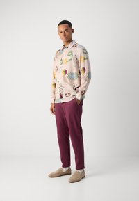 Light pink long-sleeve shirt with colorful floral patterns, paired with burgundy trousers and tan loafers, standing on a neutral background.