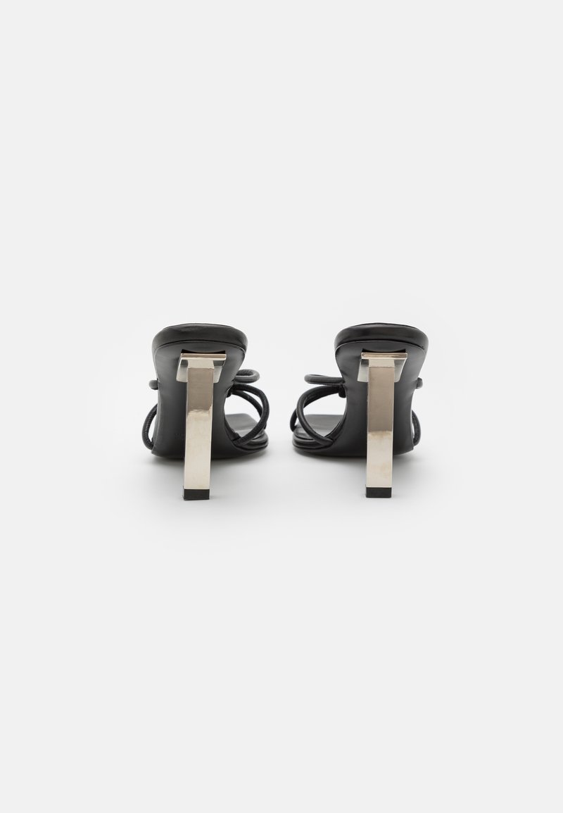 Sandali neri con tacco a spillo, presentano un design posteriore elegante, un robusto tacco a blocco metallico e cinturini elastici per una vestibilità sicura. Parte superiore in pelle liscia.