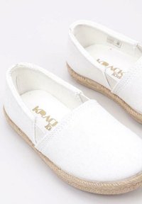 Zapatillas blancas de lona slip-on con parte superior texturizada y suela de yute. Logotipo dorado en la plantilla, punta redondeada y paneles elásticos para facilitar su uso.