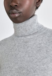 Γκρι πουλόβερ με φαρδιά λαιμόκοψη, φτιαγμένο από μαλακό πλεκτό ύφασμα, με ριμπά κολάρο και υφή. Η κοντινή λήψη εστιάζει στην περιοχή του λαιμού.