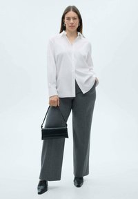 White button-up shirt, loose fit, long sleeves; gray pinstripe trousers, wide-leg style; black handbag; black pointed-toe heels.