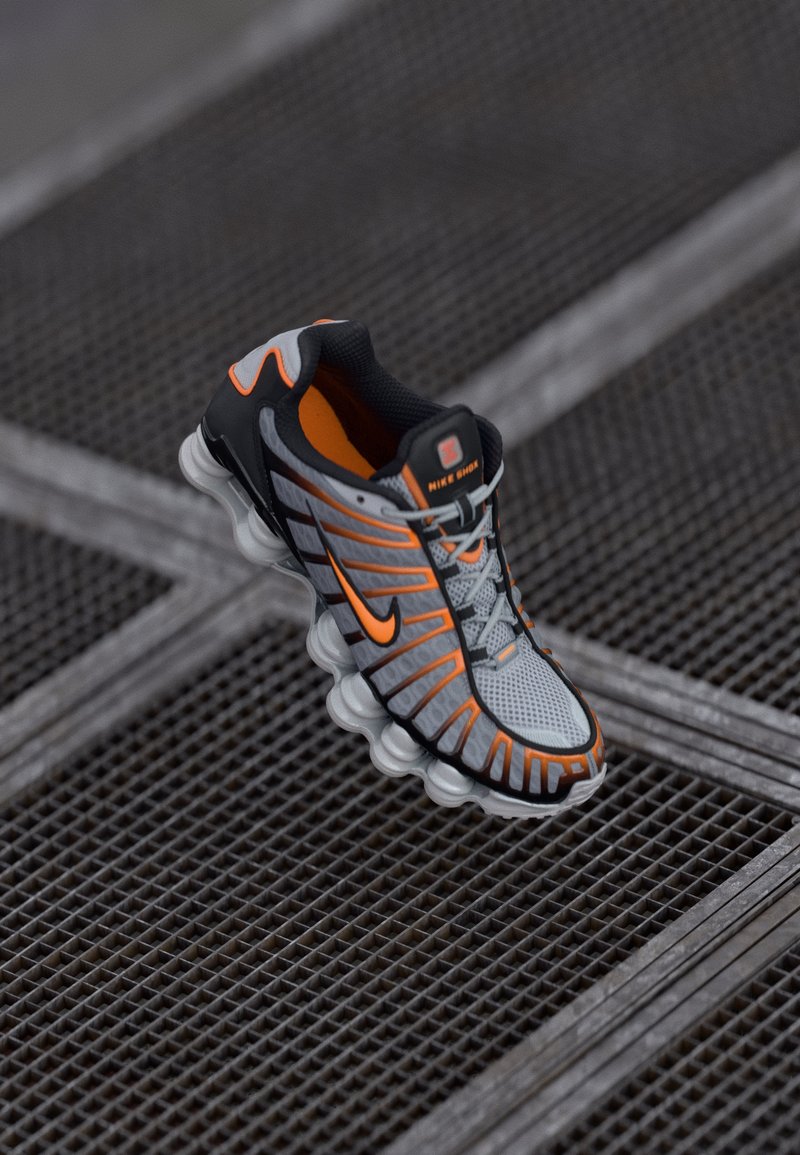 Nike running shoe with a gray mesh upper, black and orange accents, distinctive wavy sole, and reflective details for visibility.